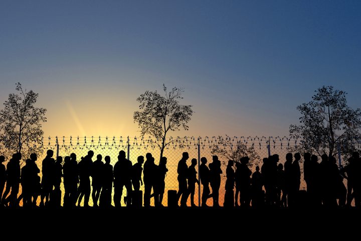 Column of migrants near the state borders. Fence and barbed wire. Surveillance, supervised. Refugees and immigrants