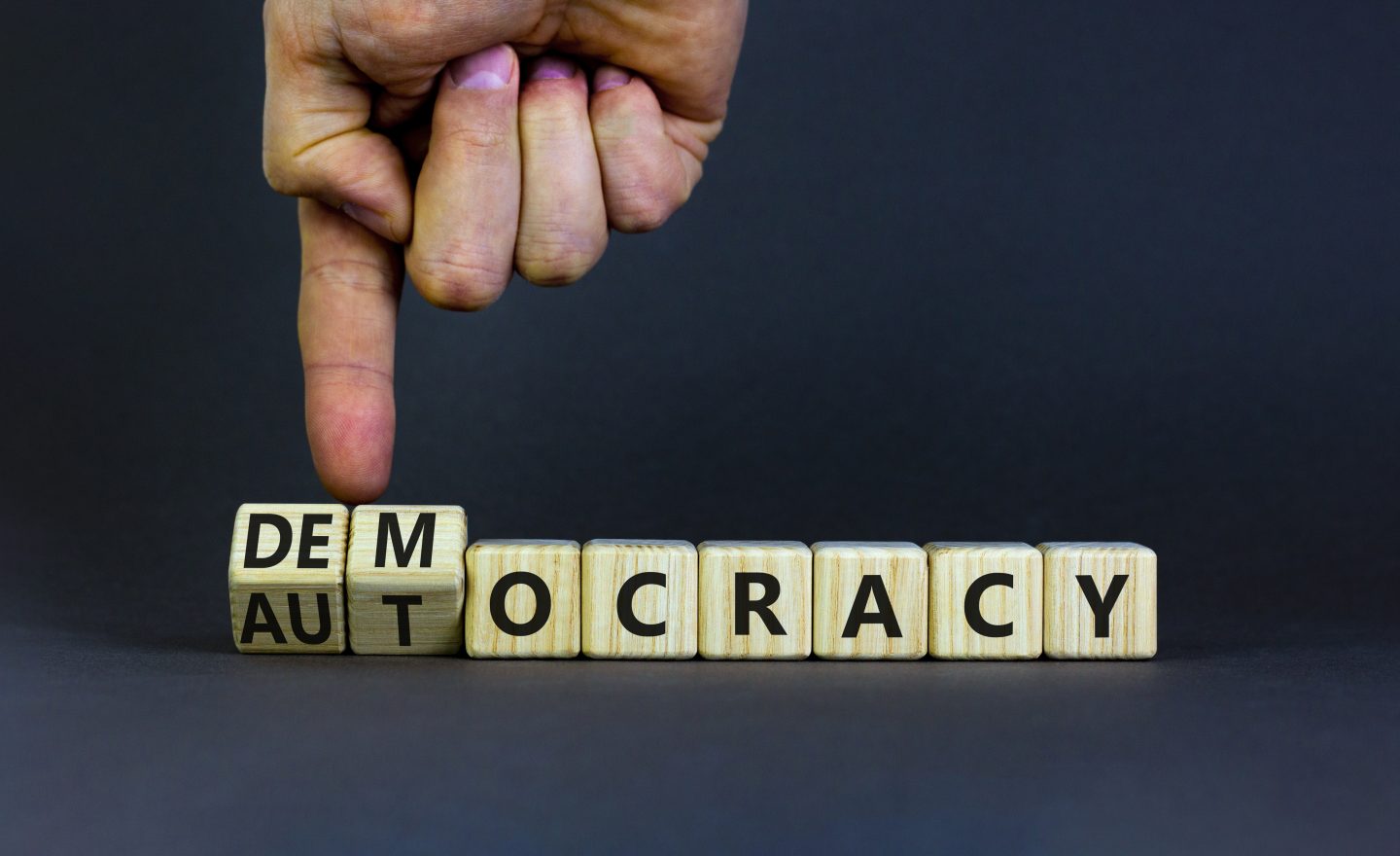 Democracy or autocracy symbol. Businessman turns wooden cubes and changes the word autocracy to democracy. Beautiful grey background, copy space. Business and democracy or autocracy concept.