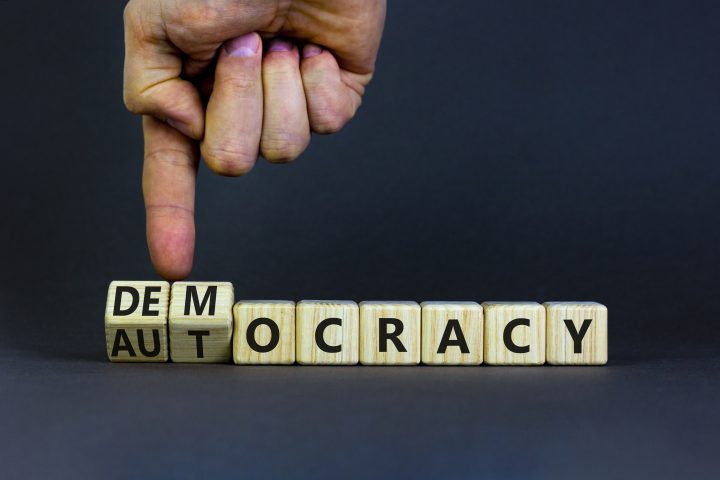 Democracy or autocracy symbol. Businessman turns wooden cubes and changes the word autocracy to democracy. Beautiful grey background, copy space. Business and democracy or autocracy concept.